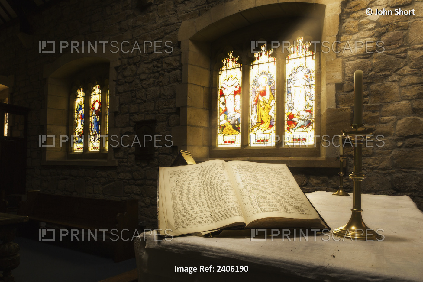 An Open Bible On Display In A Church With Colourful Stained Glass Windows; ...