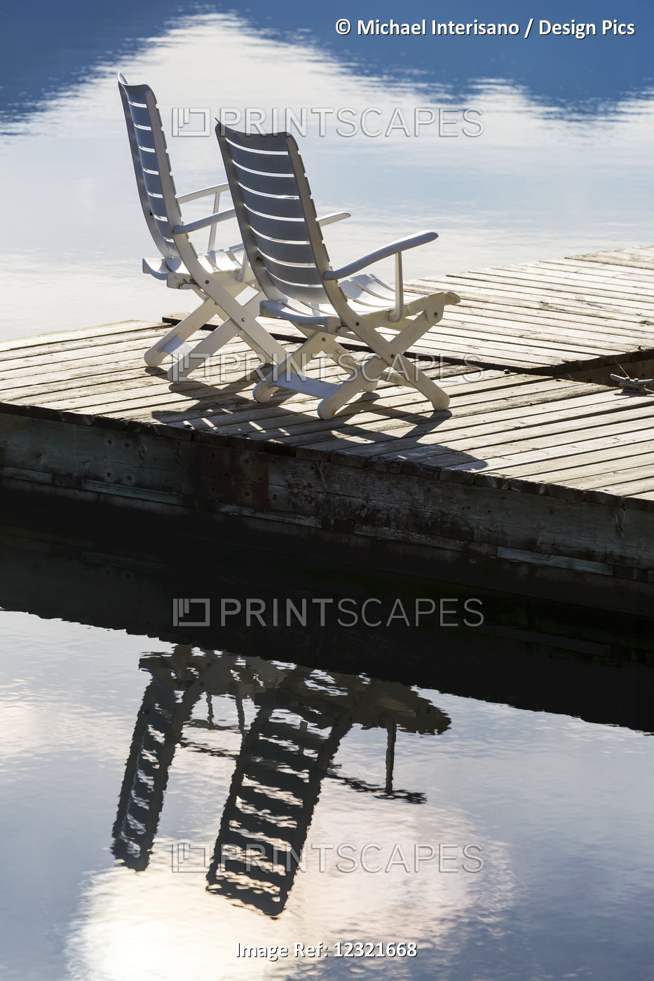 Two White Wooden Deck Chairs On Wooden Boat Dock Reflecting In The Water; ...