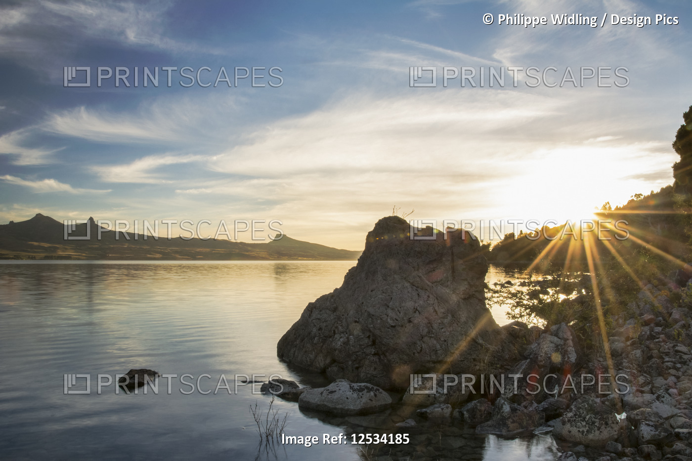 The sun rising on a lake causing a sunburst on the righthand side of the image; ...