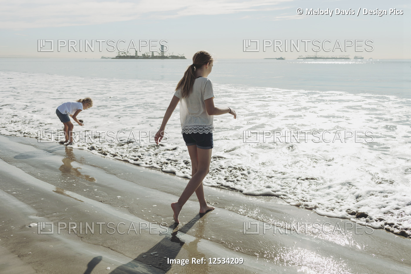 Two sisters walking out to the surf on a beach; Long Beach, California, United ...