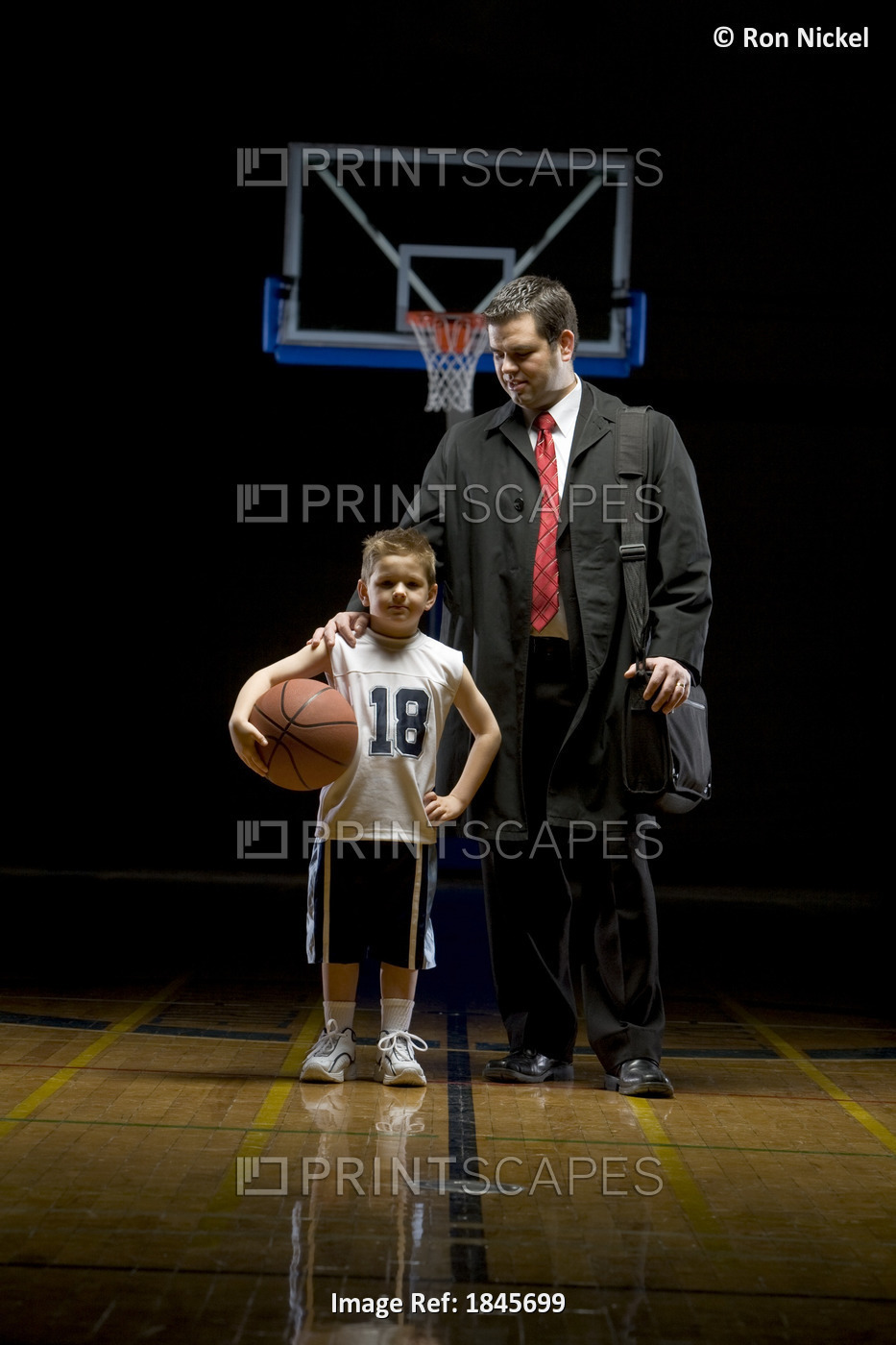 Young Boy Standing On Basketball Court With His Father