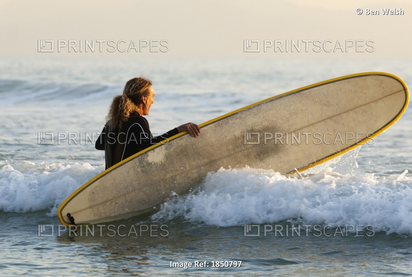 Female Surfer Wading Into Ocean With Surfboard