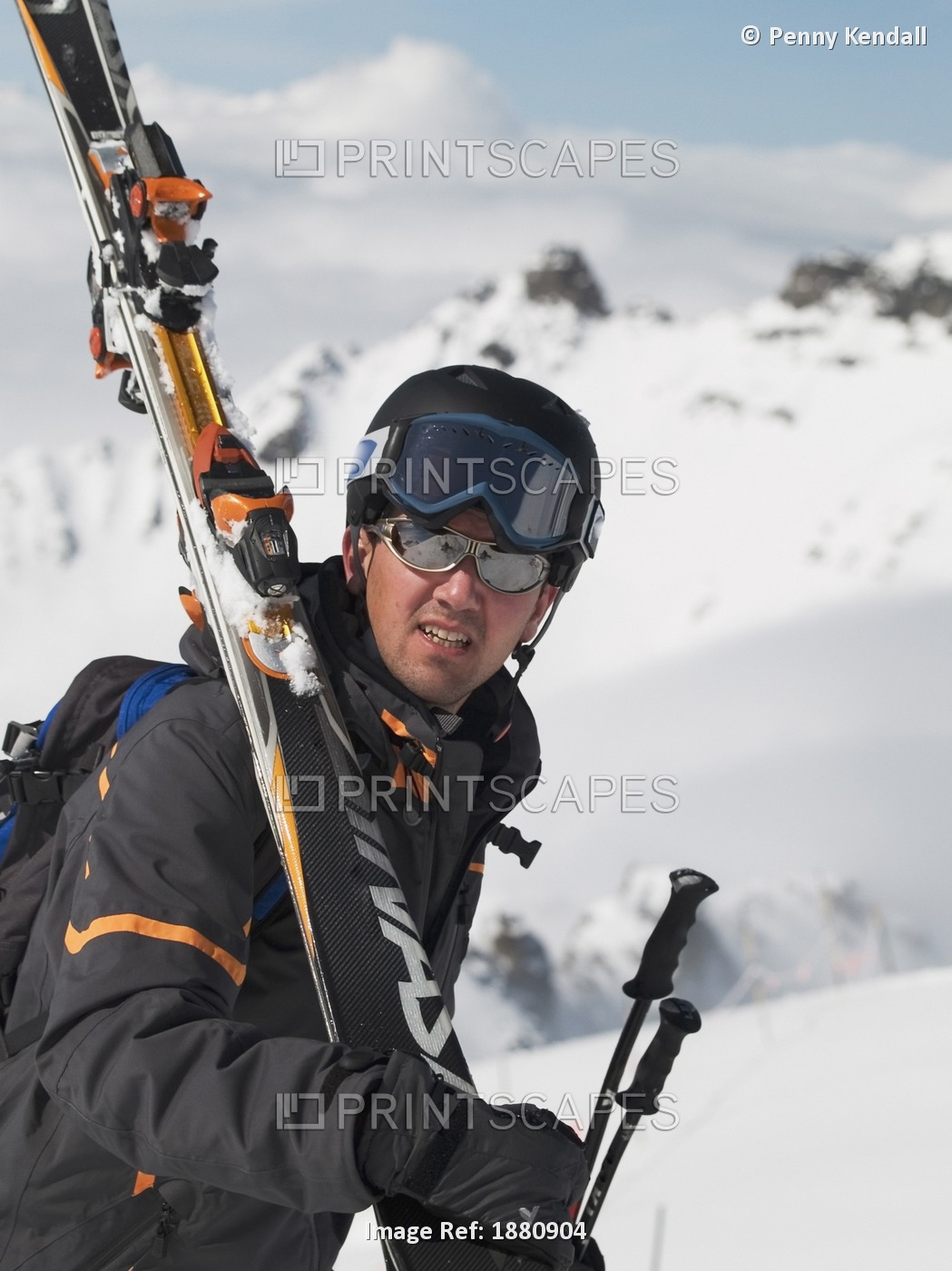 Portrait Of Male Helmeted Skier With Goggles Carrying Skis Over Shoulder