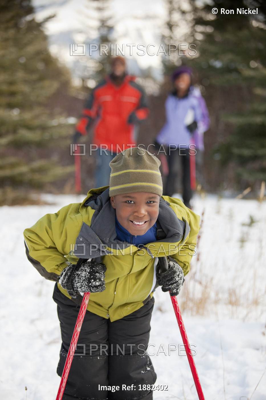 A Boy Holding Ski Poles With His Parents In The Background; Lake Louise, ...