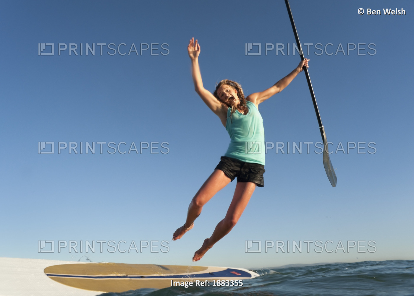 A Woman Jumps Into The Water Off A Surf Board While Holding Her Paddle In Front ...