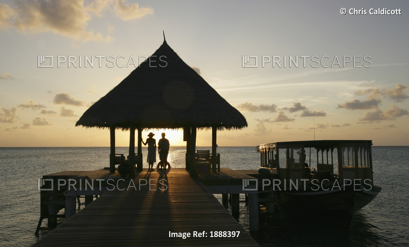 Couple On Pier Watching The Sunset.