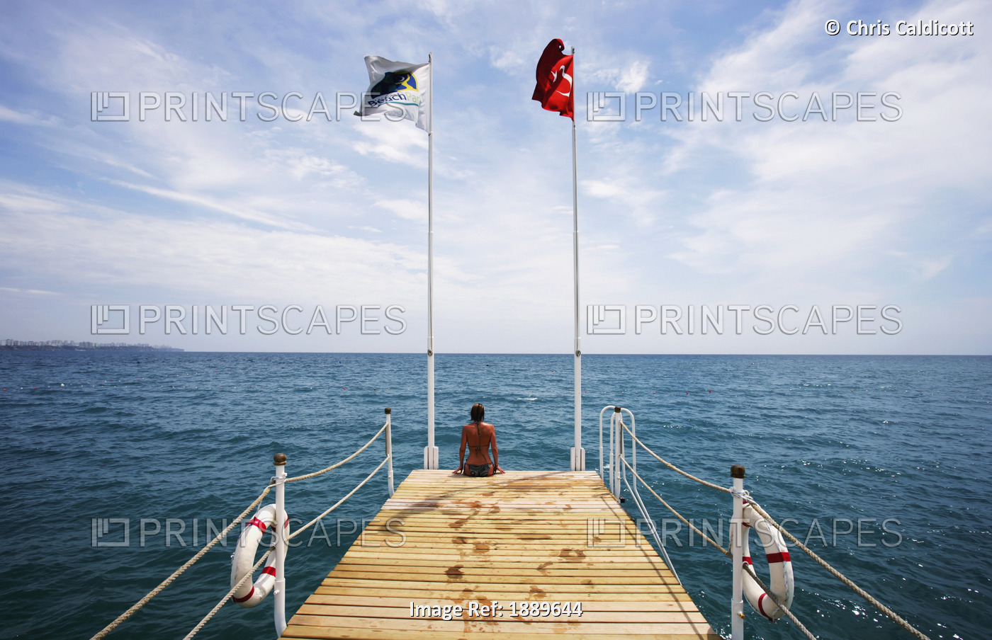 Woman Sitting On Pier With Flags And Life Rings