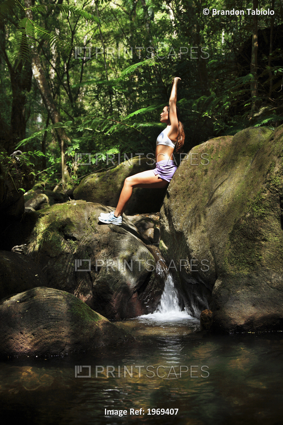 Hawaii, Oahu, Young Female Doing Yoga In A Lush Forest With Waterfall Below Her.
