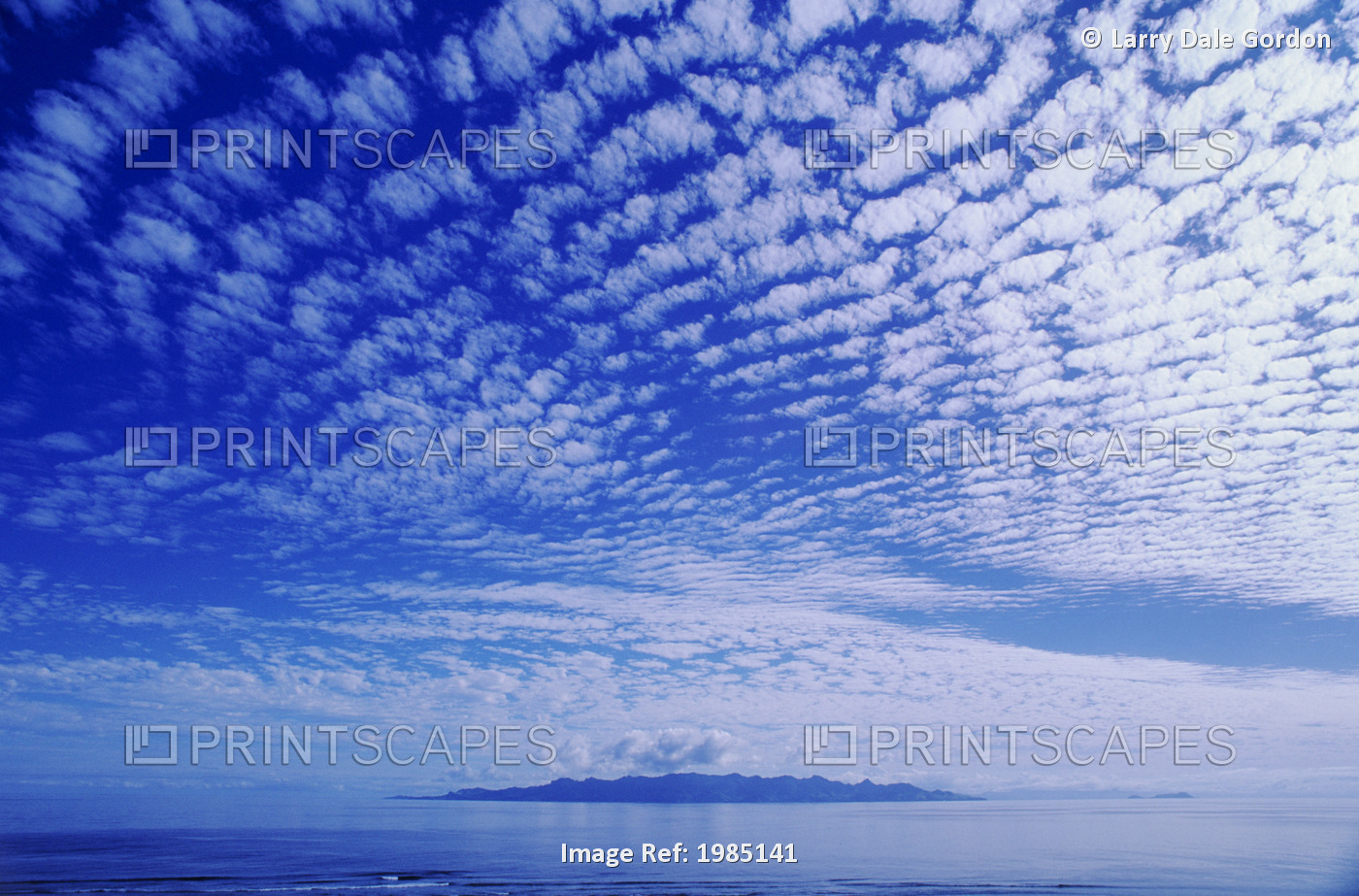 Cotton-Like Clouds In Blue Sky Over Smooth Ocean Water, Island In Distance.