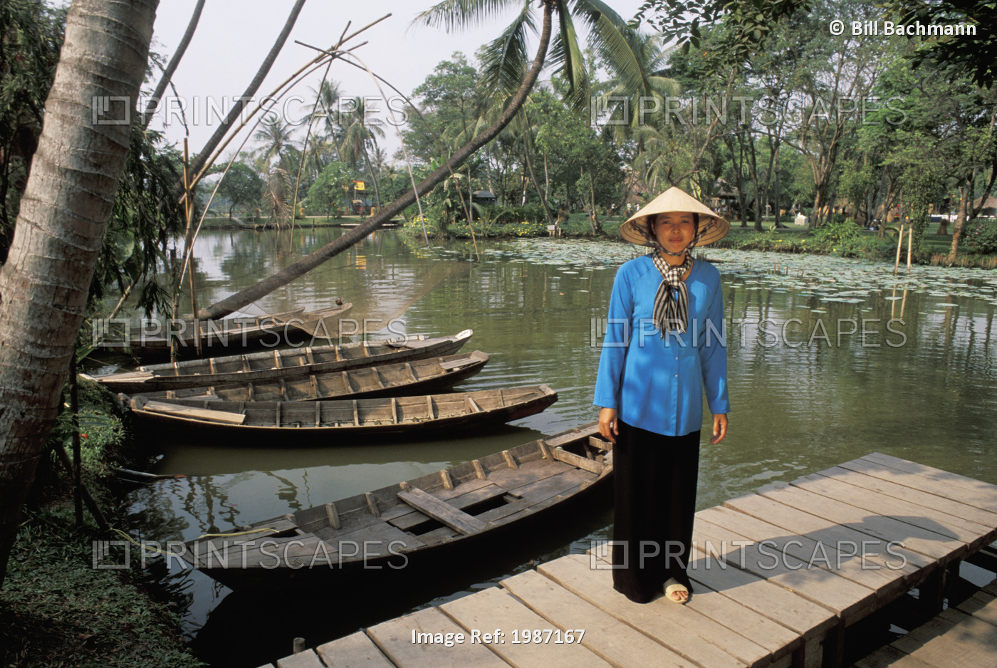 Vietnam, Woman in traditional clothing standing on dock near river and old ...