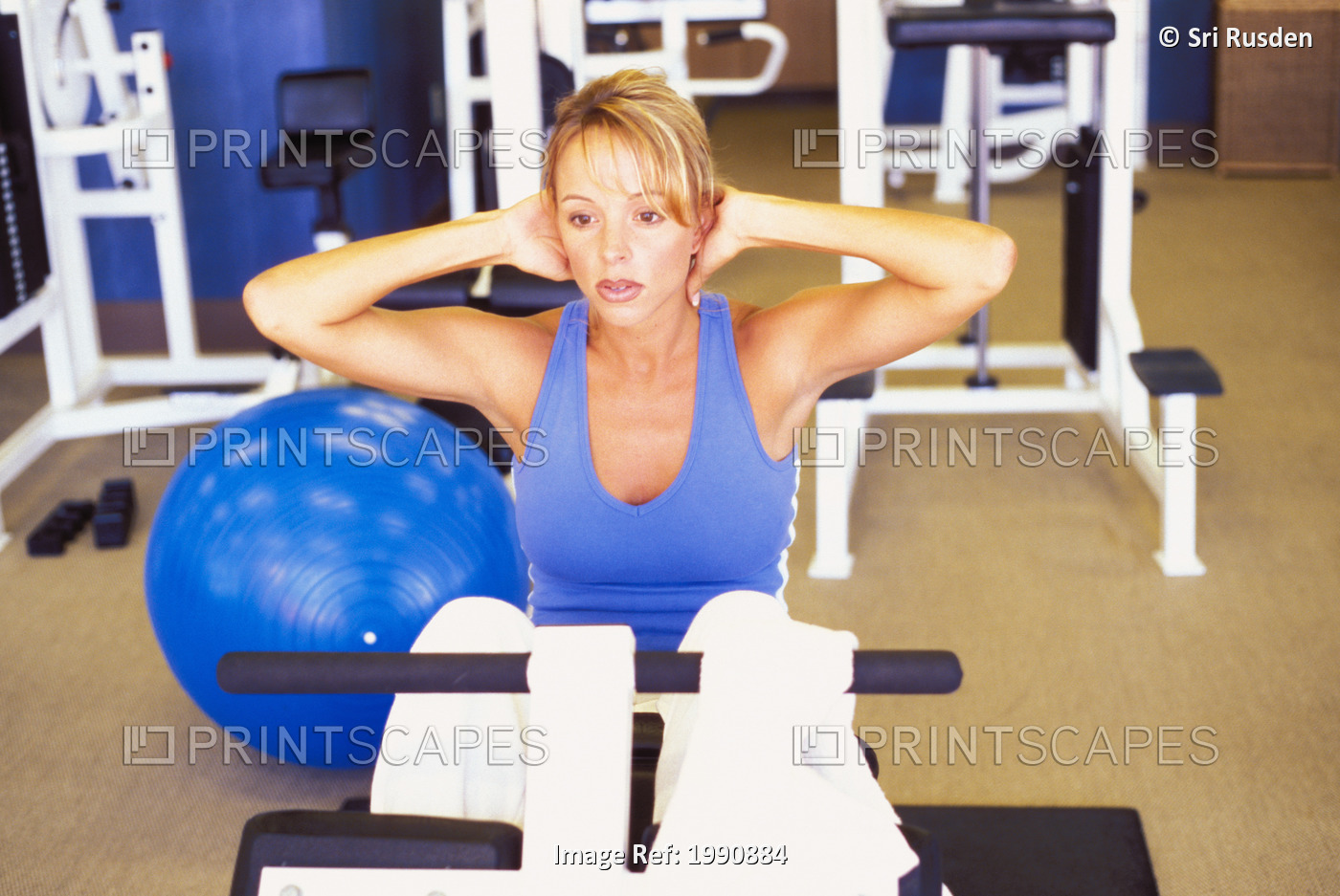Blond Woman Sitting On Exercise Equipment Working On Her Abdominal Muscles