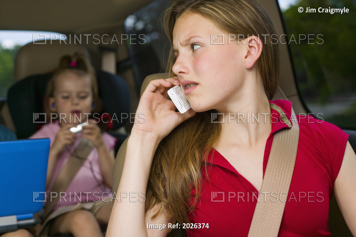 Annoyed Teenager Using Cell Phone With Siblings In The Background Playing With ...
