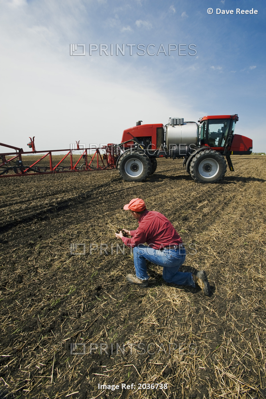 A Man Examines Newly Seeded Soil Next To A High Clearance Sprayer Being Used To ...