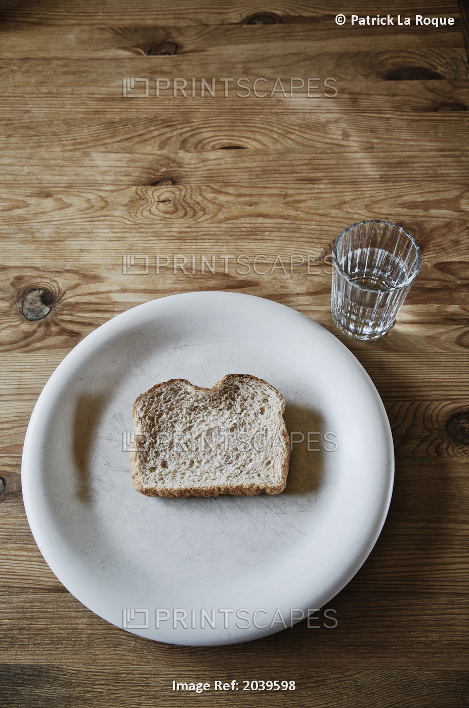 Slice Of Stale Bread On A White Plate With A Glass Of Water