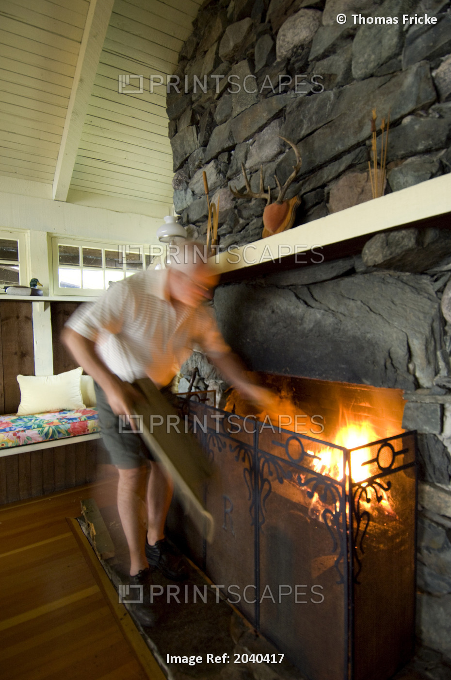 Man Putting Logs In Cottage Fireplace, Lake Of The Woods, Kenora, Ontario