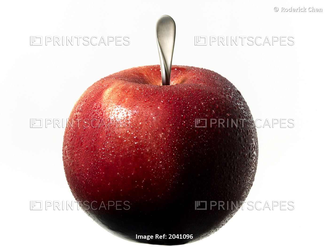 A Fresh Apple With A Silver Spoon Handle For The Stem On A White Background