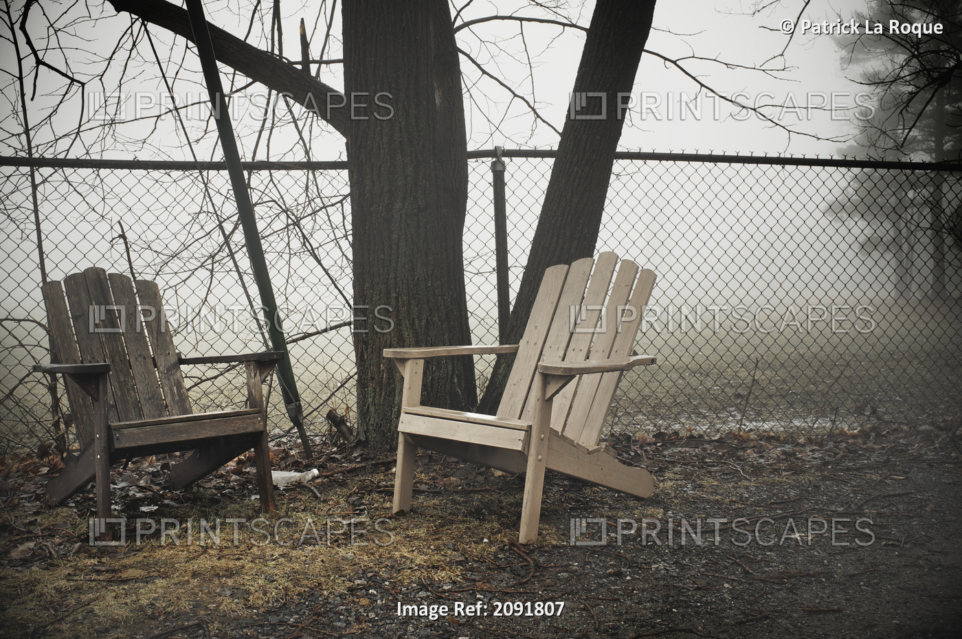 Two Wooden Adirondack Chairs By A Steel Fence On A Foggy Day; Otterburn Park, ...