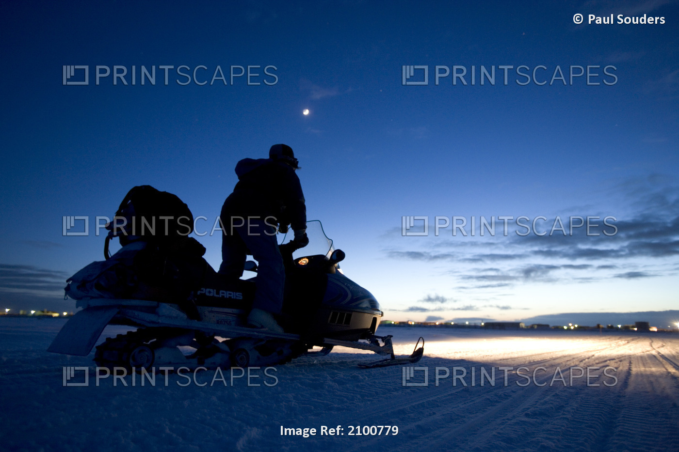 Man Rides A Snowmobile On Sea Ice Under Crescent Moon At Dusk Along The Bering ...