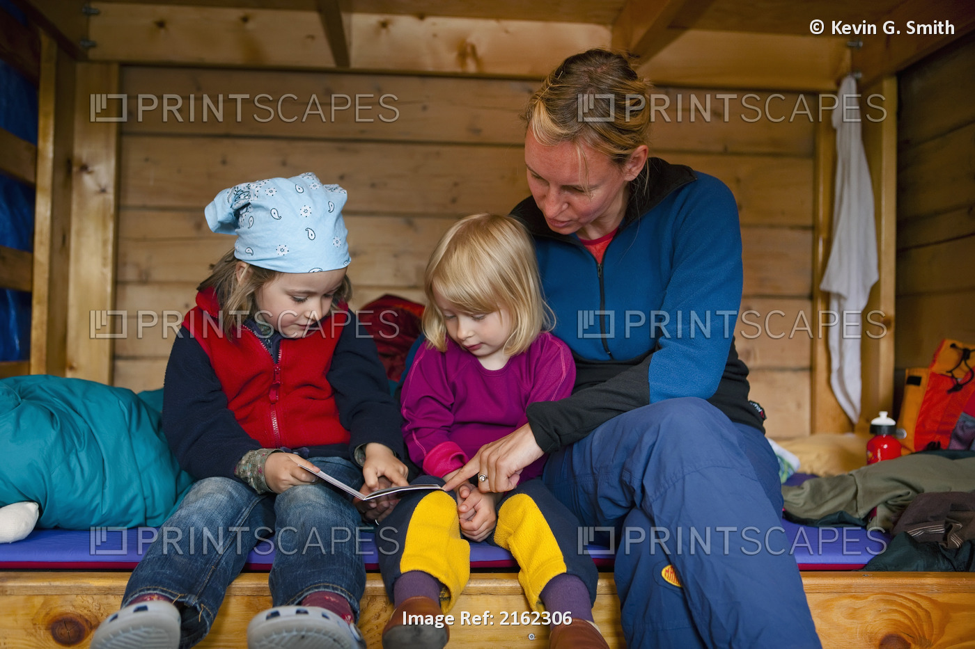 Mother And Young Daughters Sit On A Bunk Bed In A Cabin Reading A Story, ...