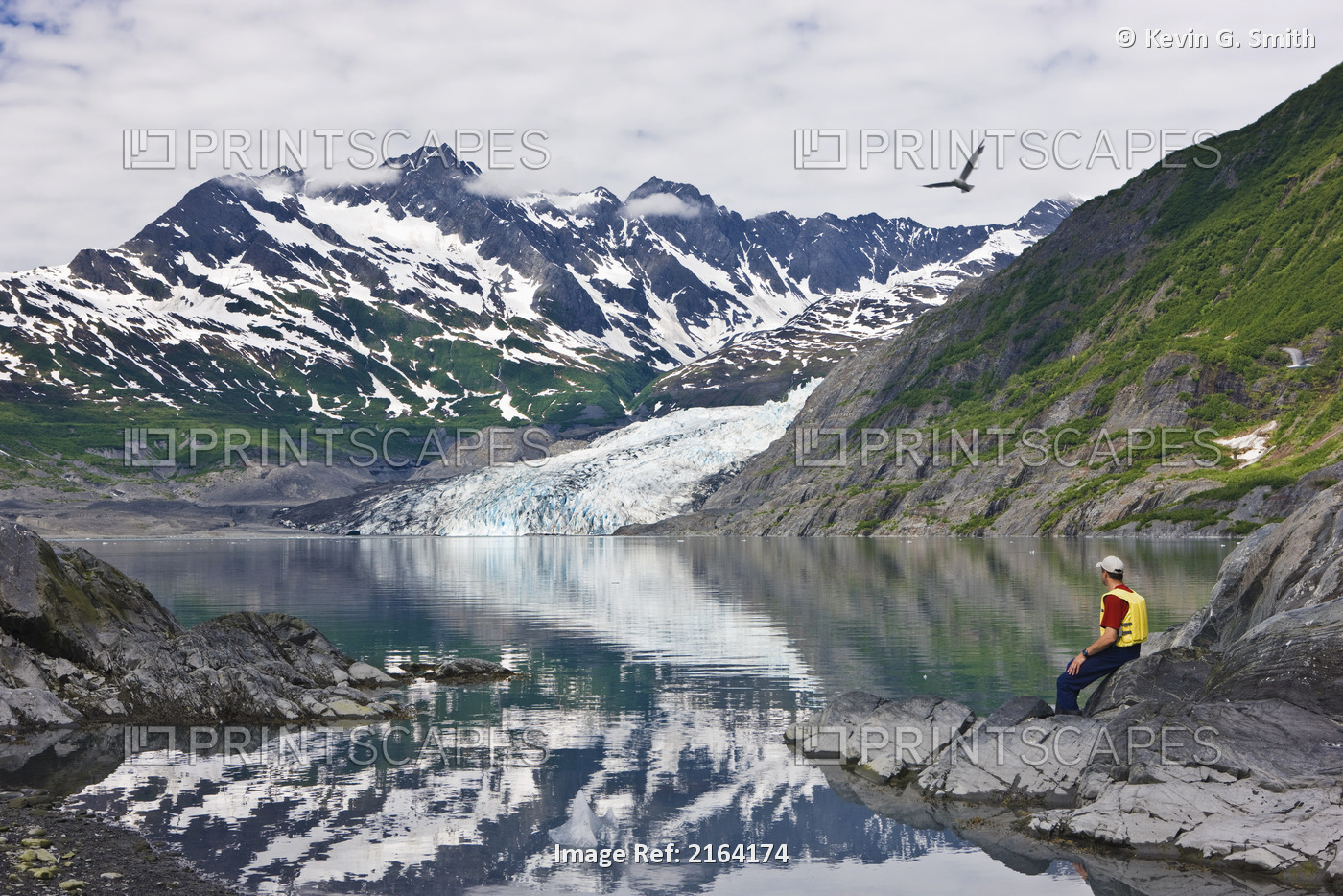 Male Sea Kayaker Sitting On An Island, Looking At Shoup Glacier Reflected In ...