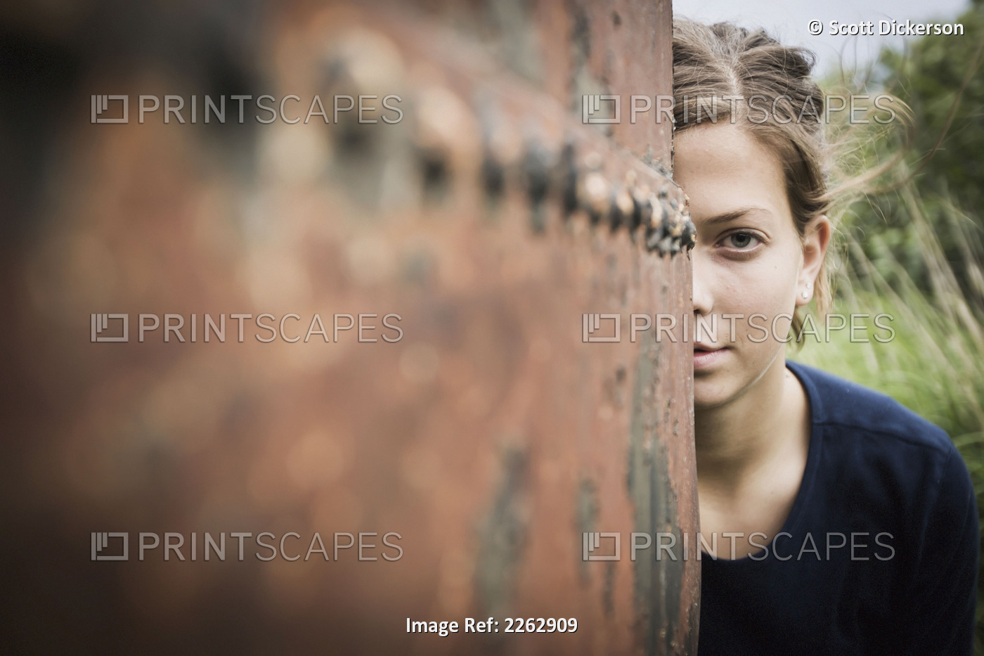 A young woman poses while peering out from behind a rusty weathered drum; South ...