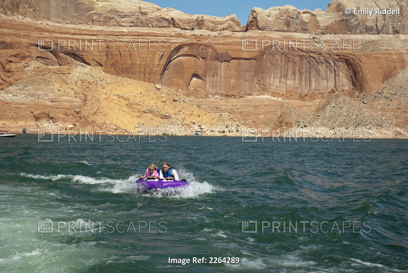 Mother and daughter ride on purple towable tube behind speedboat on lake ...