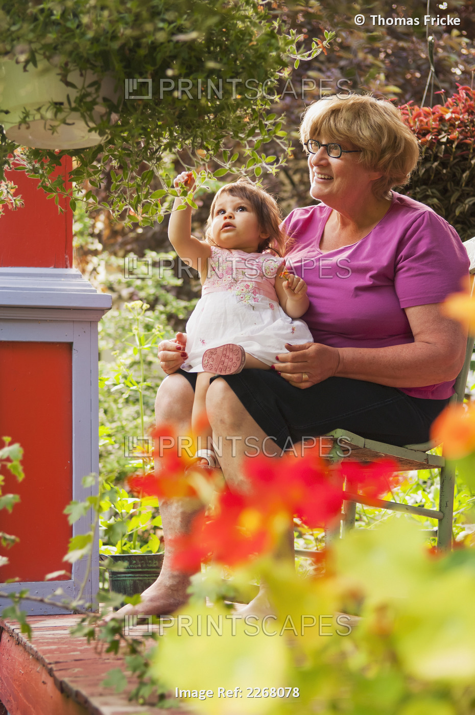 Grandmother And Child Sitting On Front Porch With Many Plants Surrounding Them; ...