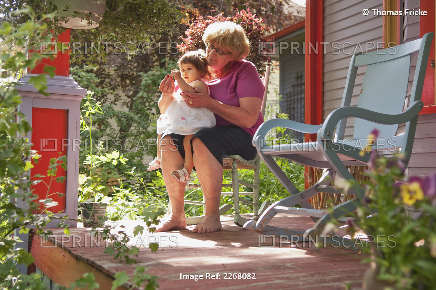Grandmother And Child Sitting On Front Porch With Many Plants Surrounding Them; ...