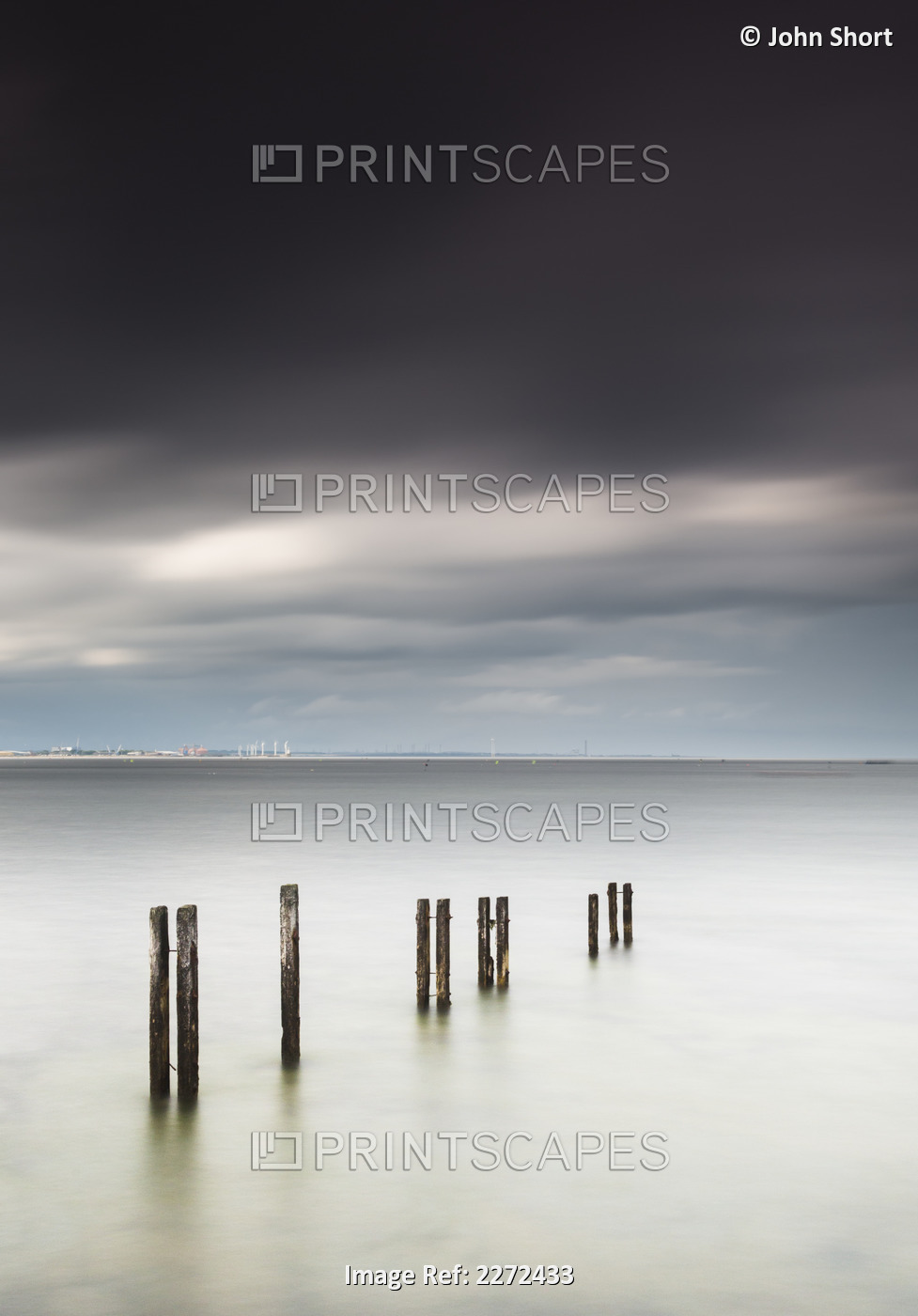Wooden posts in a row in the shallow water along the coast with a view of a ...