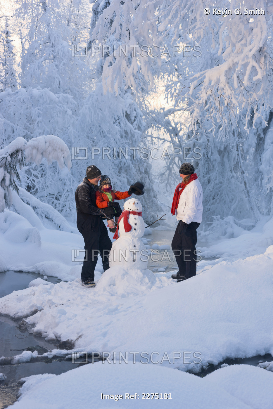 Family Putting A Top Hat On A Snowman Next To A Small Stream In A Hoarfrost ...