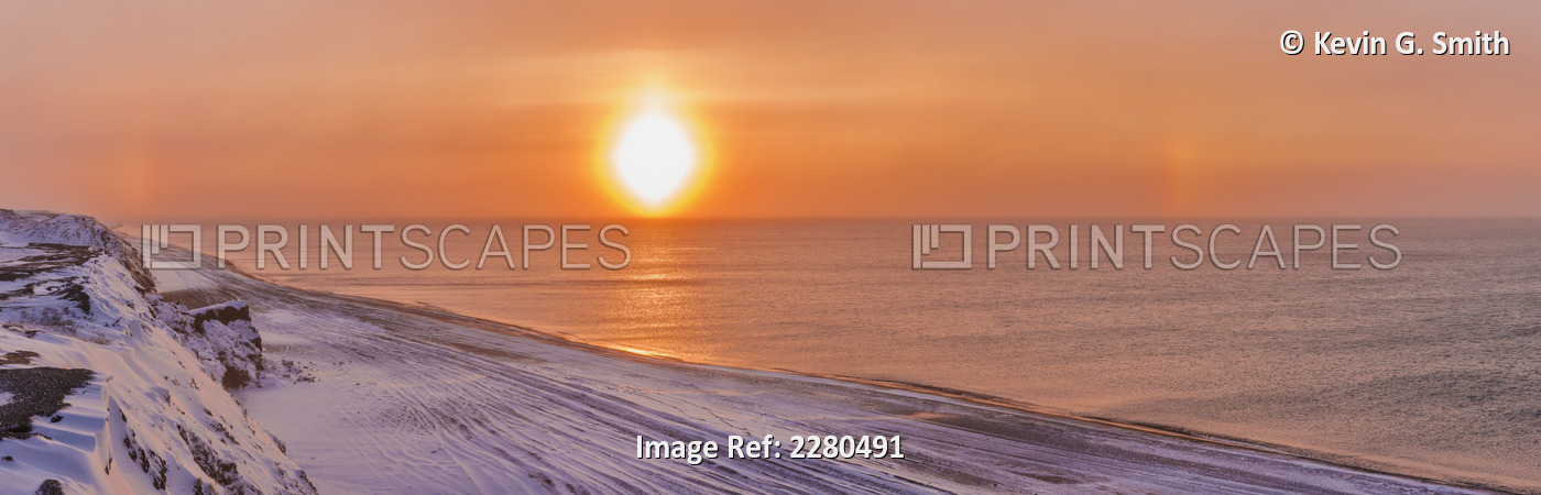 Sunset through windblown snow creates a sundog above the Beaufort Sea along the ...