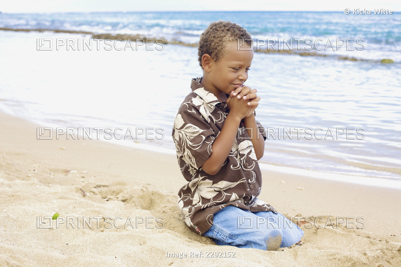 A young boy with hands folded in prayer by the ocean; Hawaii united states of ...
