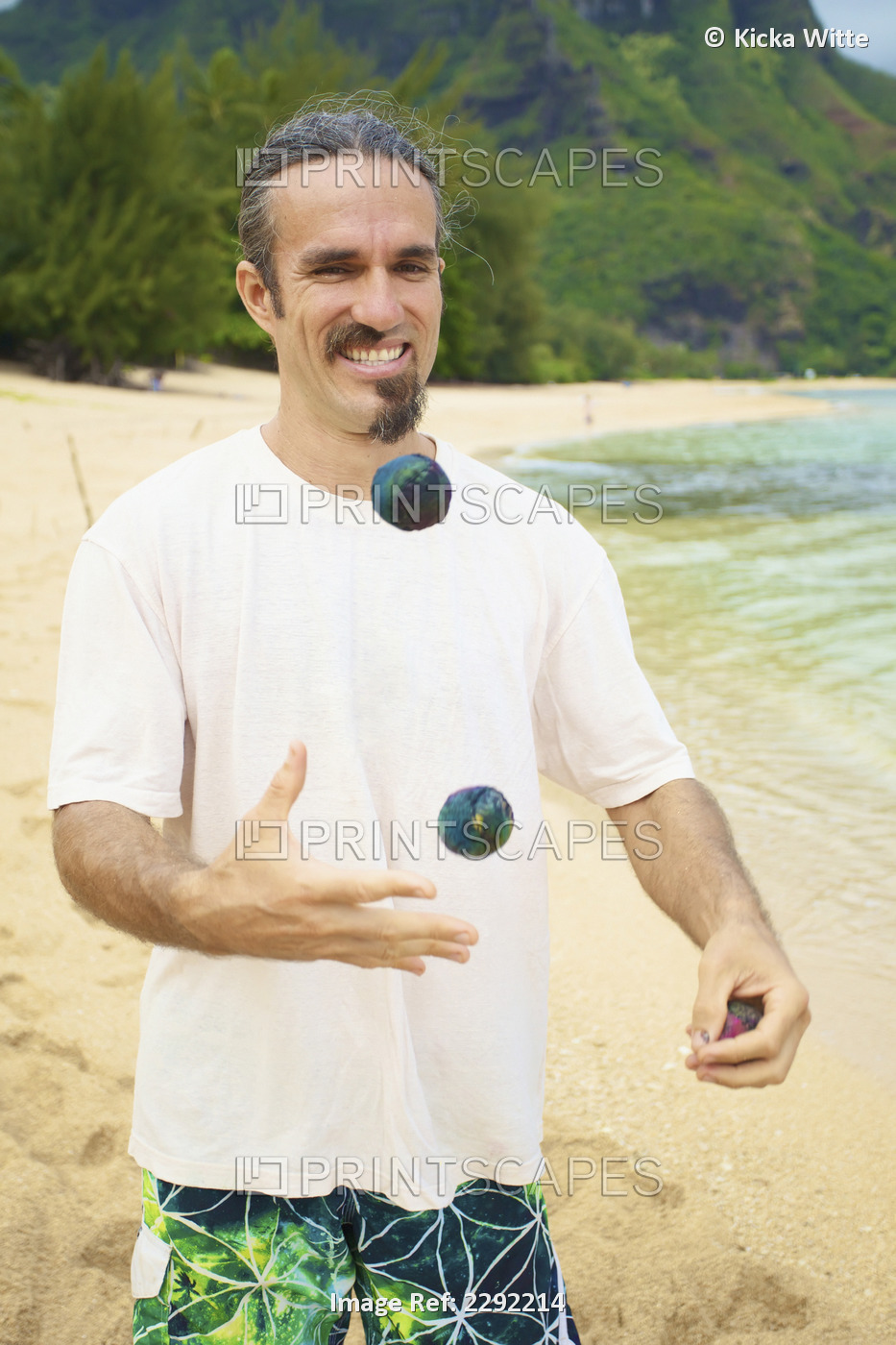 A man juggles with hackey sacks while standing on the beach at the water's ...