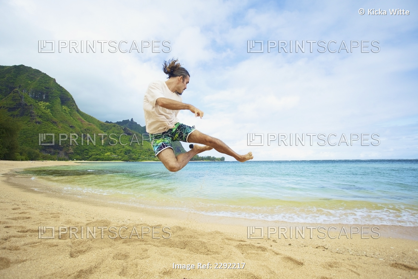 A man takes a leap into the air while playing with a hackey sack on the beach; ...
