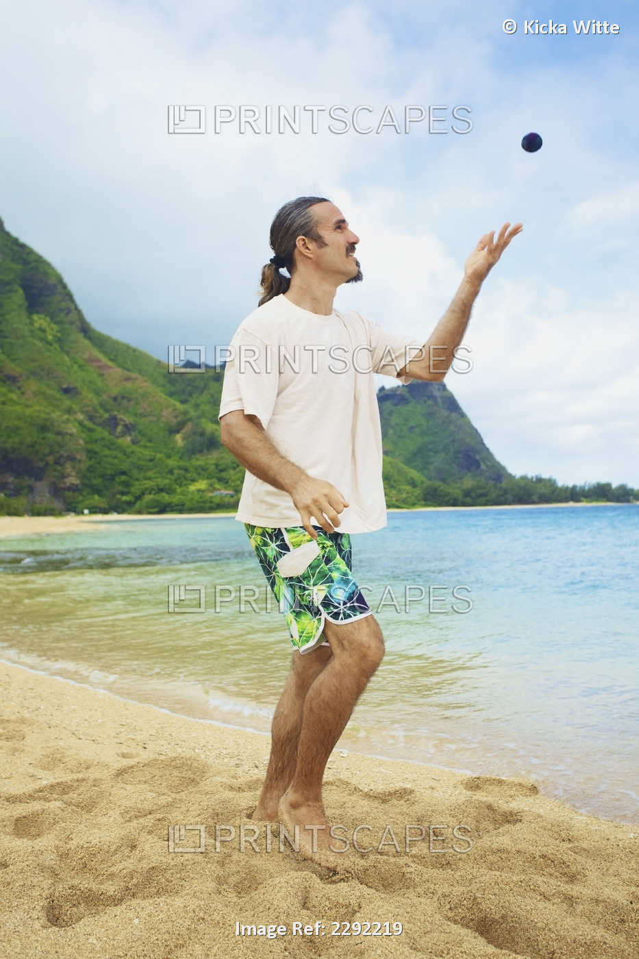 A man throws his hackey sack into the air while standing in the sand at the ...