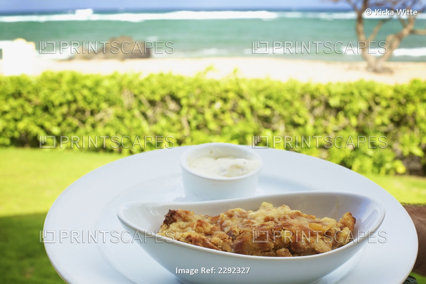 A food item served in a white serving dish with a view of the beach and ocean; ...