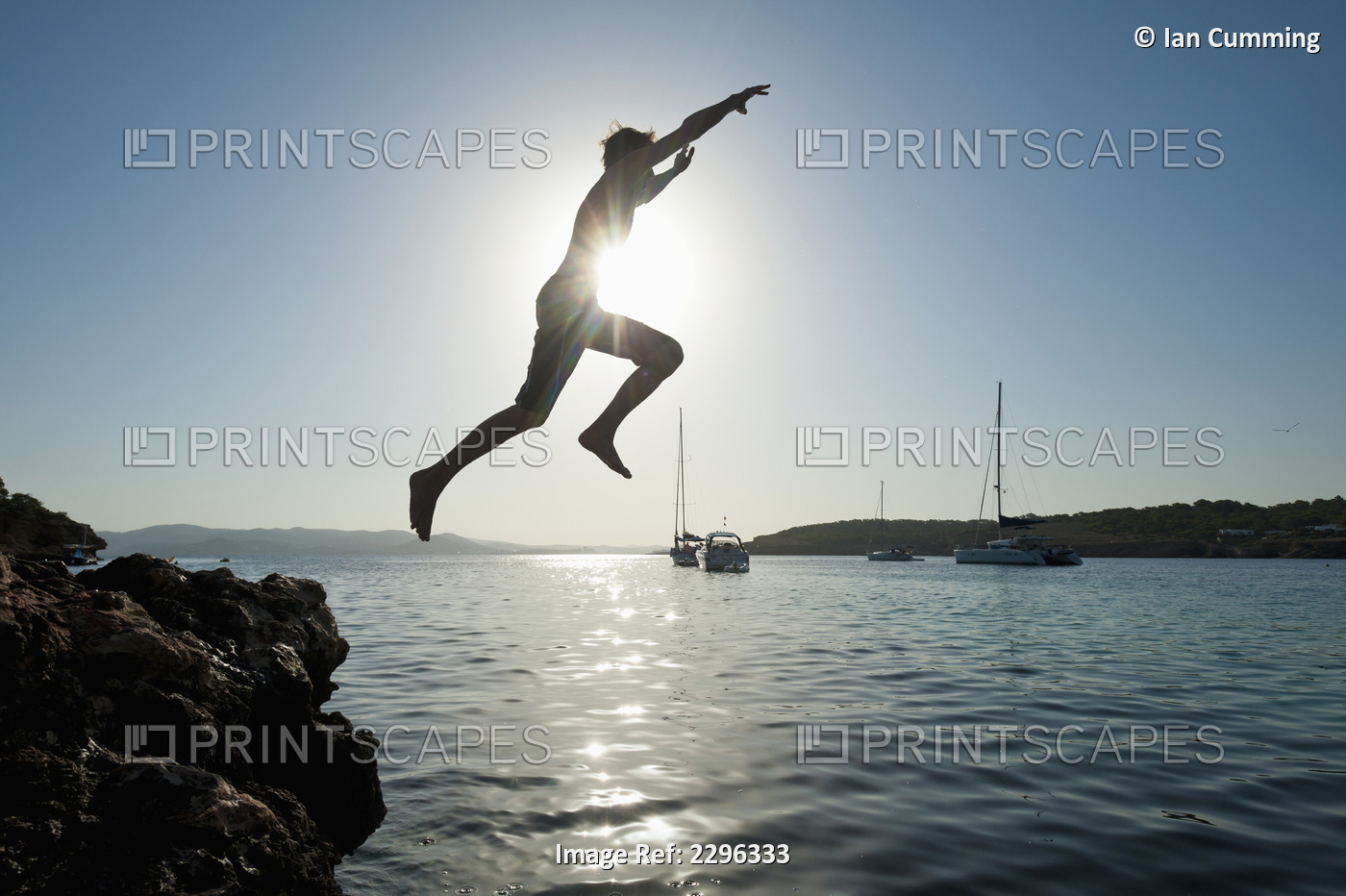 Spain, Man jumping off rocks into sea beside La Basse beach; Ibiza