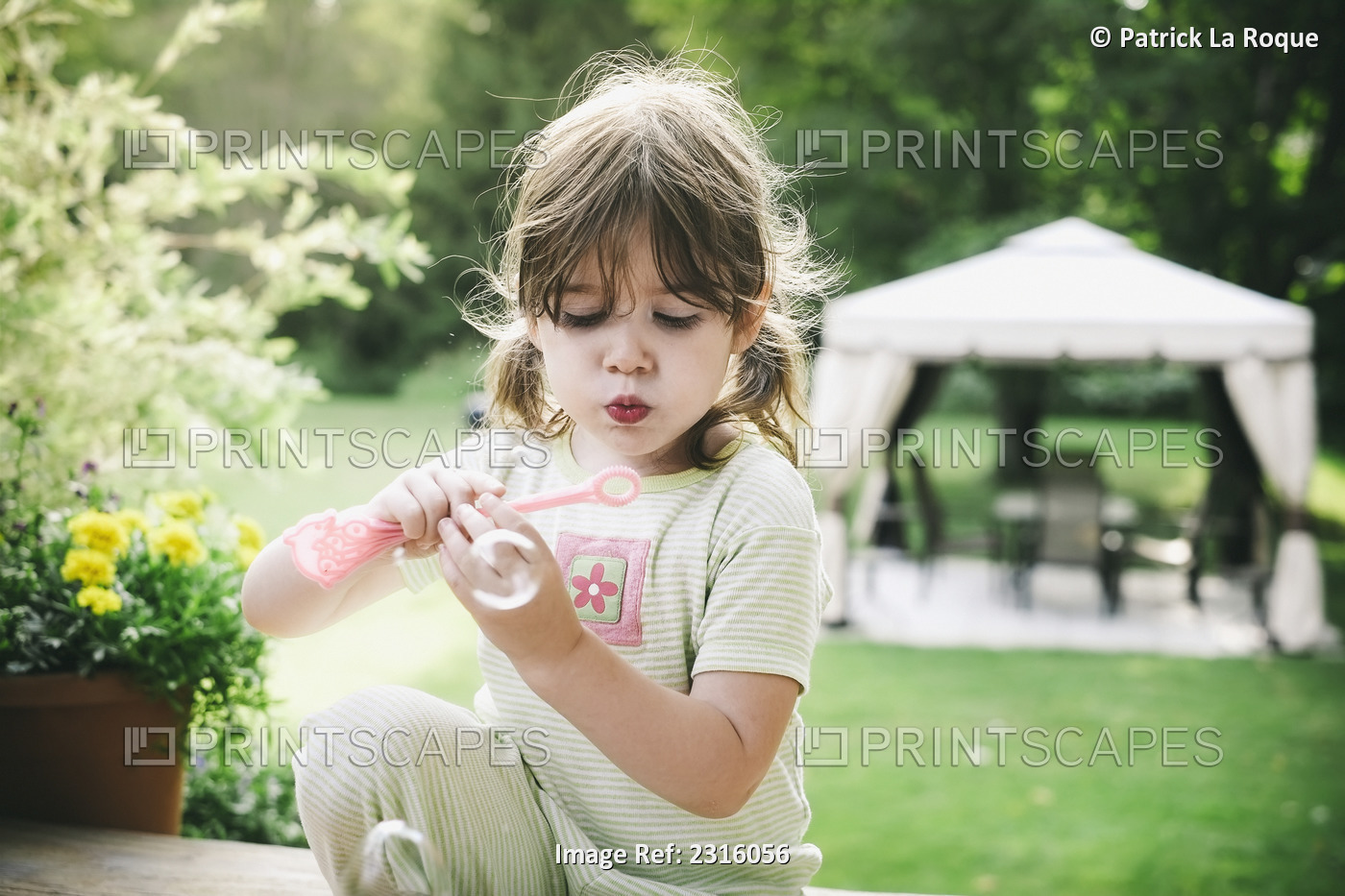 Young Girl Blowing Bubbles Outside In Her Pyjamas On A Summer Morning; ...