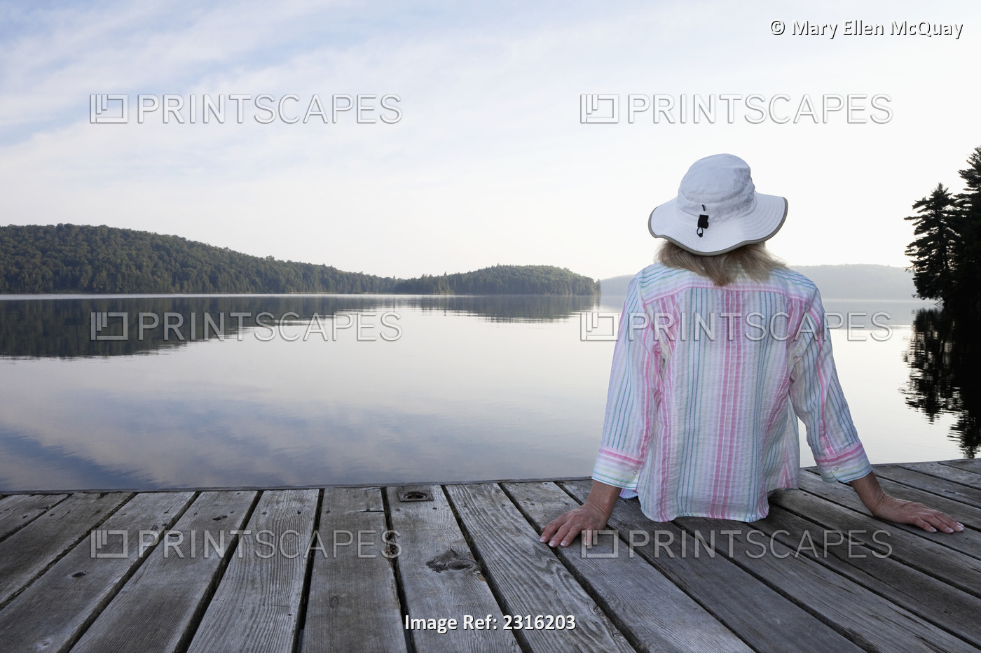 Senior Woman Sitting On Her Cottage Dock Looking Out At Lake In Algonquin Park; ...