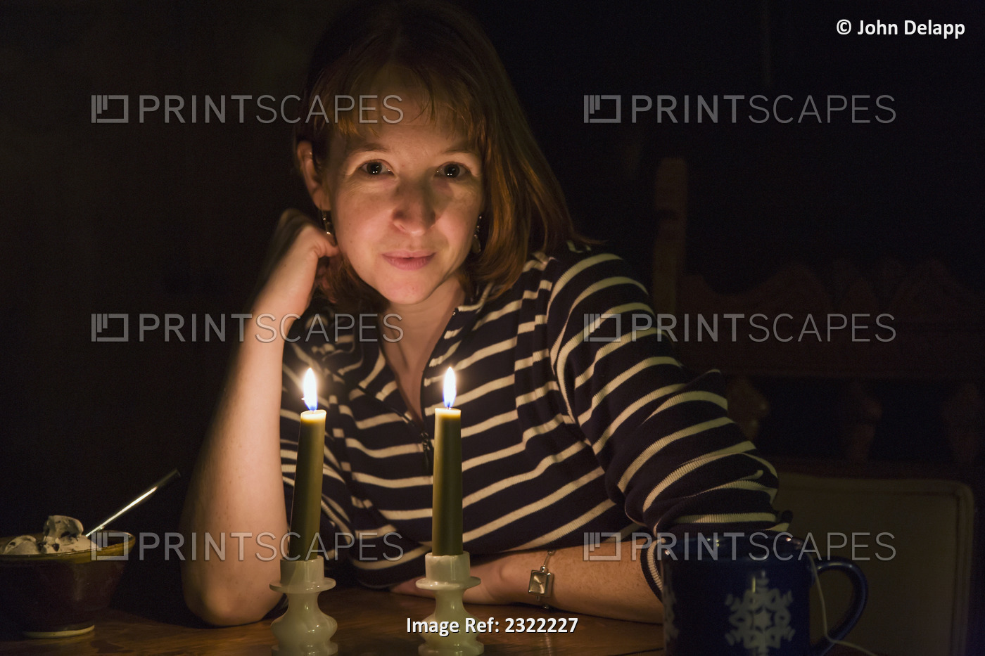 A woman sitting at a table in a dark room with a coffee cup and a bowl of ice ...