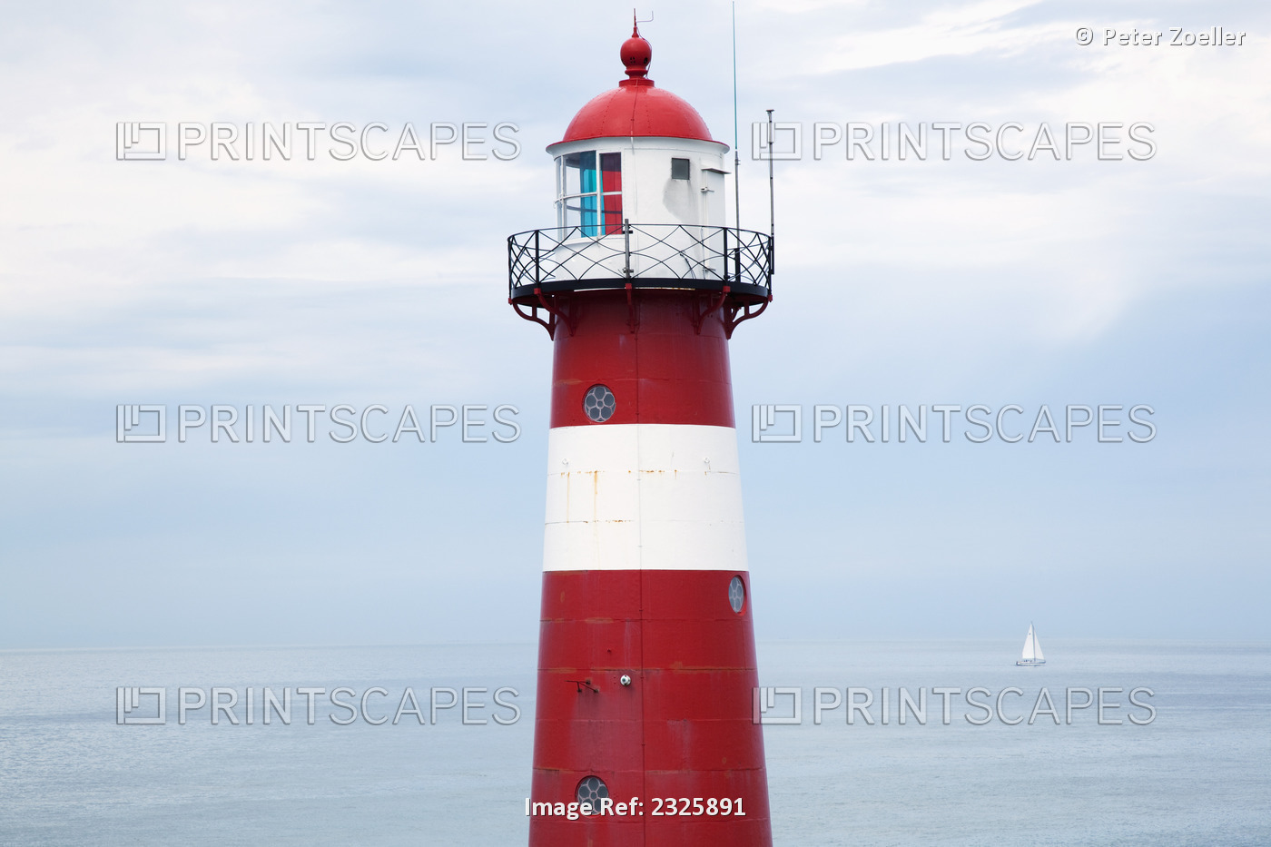 Red and white lighthouse along the coast with a sailboat in the distance near ...