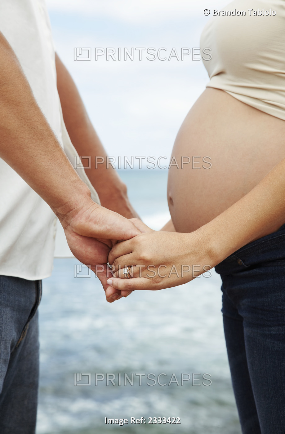 A pregnant woman and her husband hold hands at the water's edge; Honolulu ...