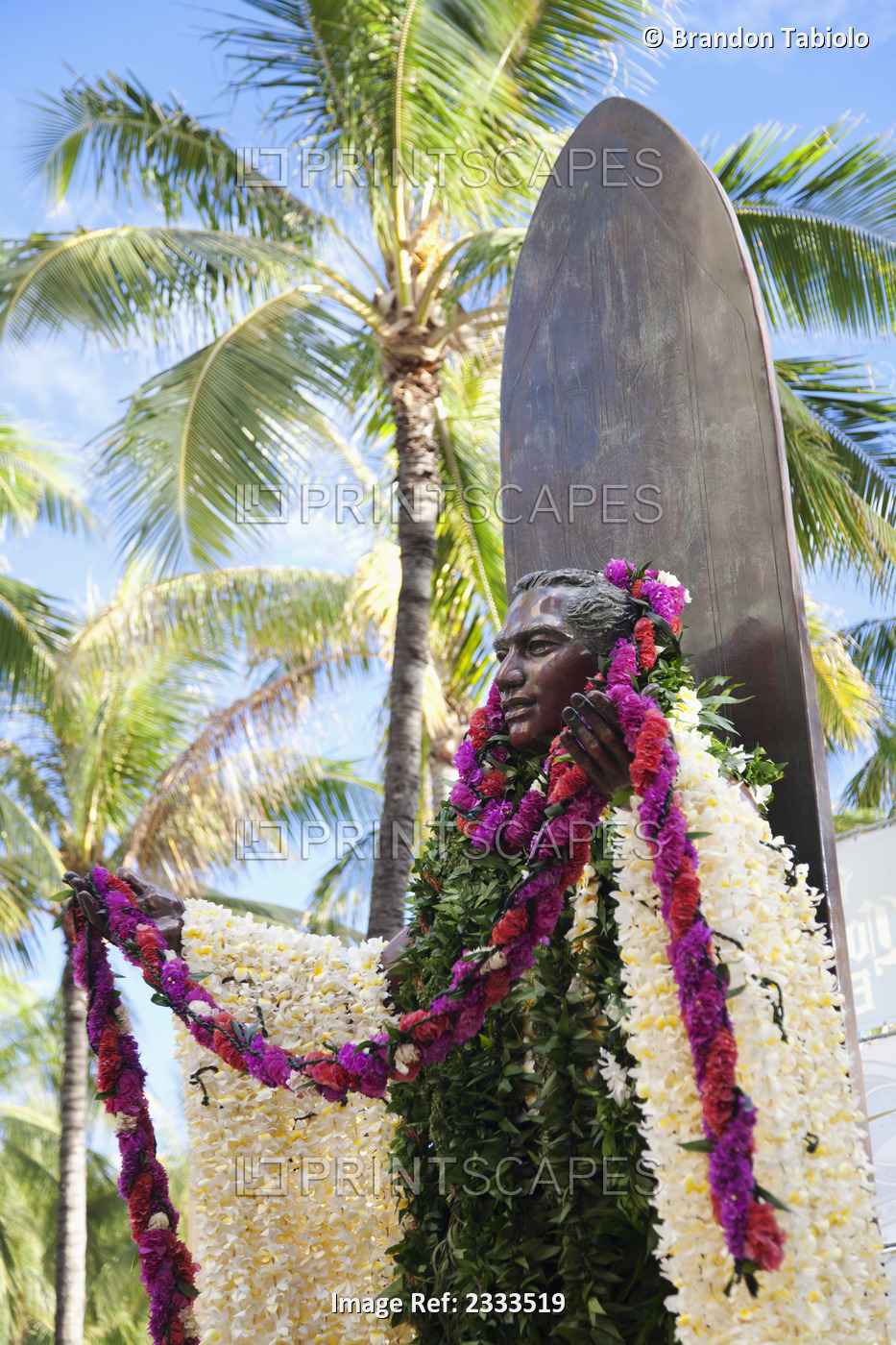 Statue Of A Man Covered In Floral Leis Standing Against A Surfboard; Honolulu, ...