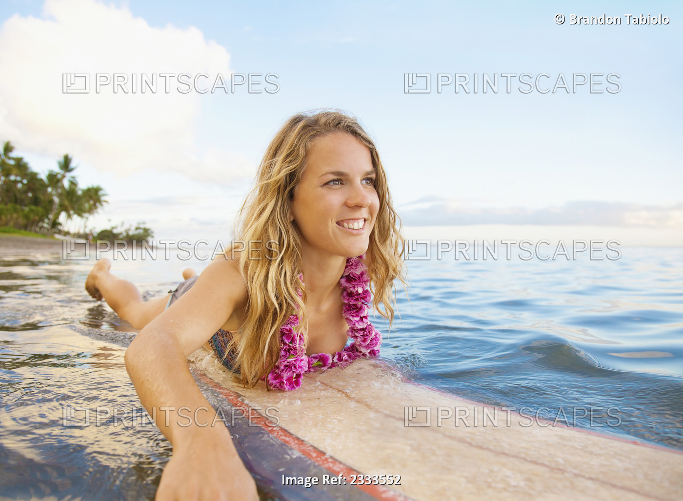 A Young Woman Wearing A Lei Rides A Surfboard Out In The Water; Maui, Hawaii, ...