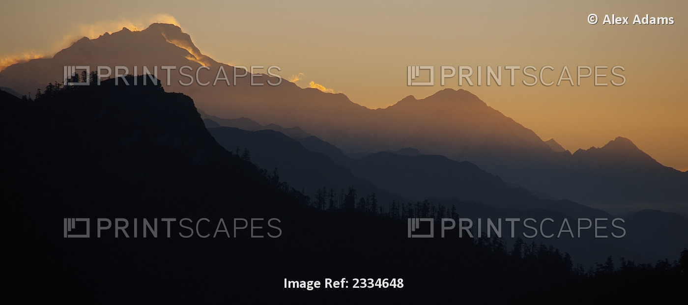 Silhouette of a mountainous landscape with a glowing sky behind it at sunset ...