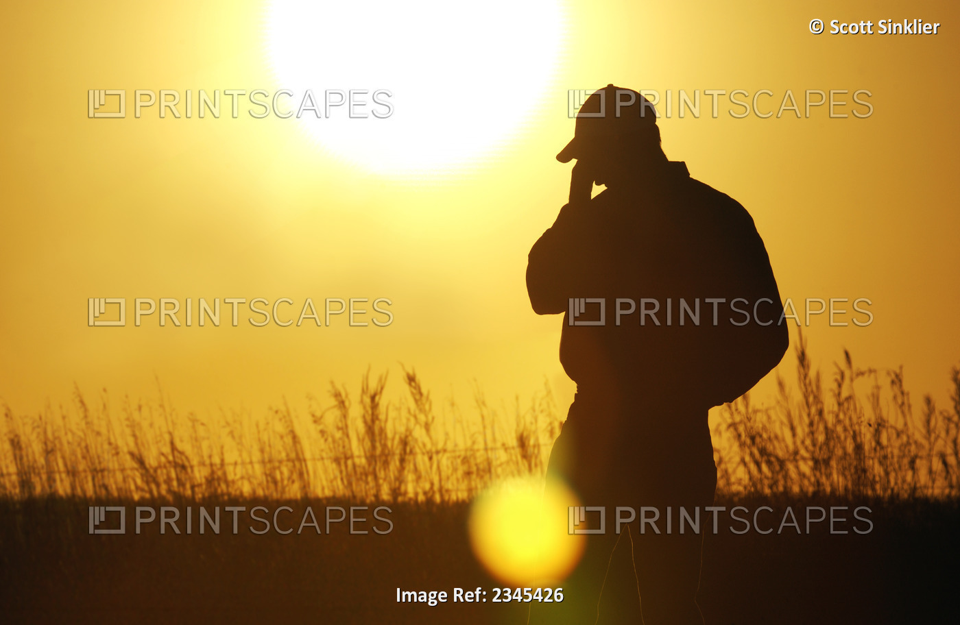 Agriculture - A farmer, silhouetted by the setting sun, talks on a cell phone ...