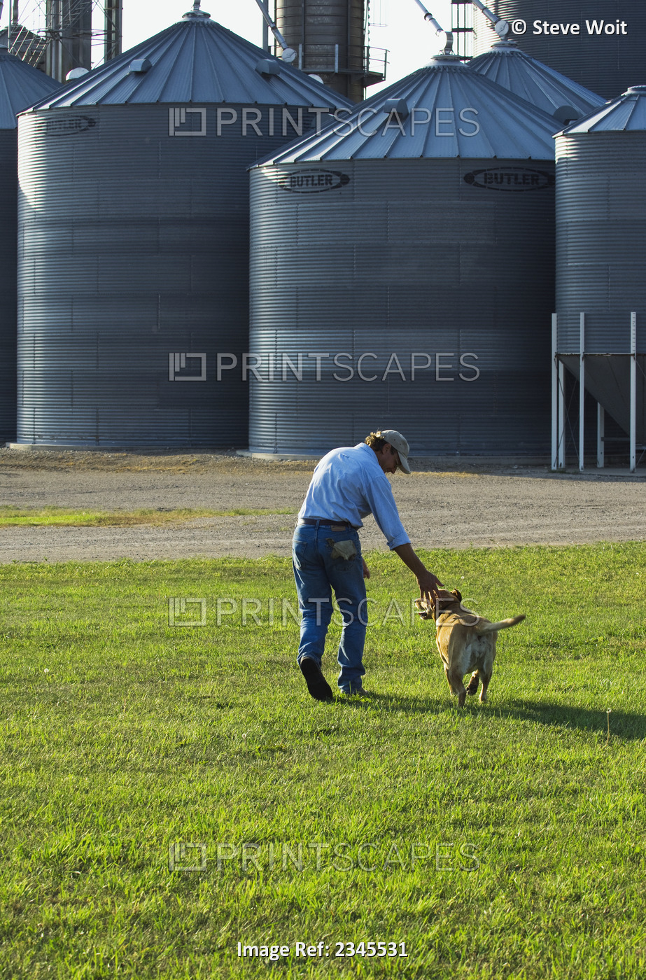 Agriculture - A farmer plays with his dog at the end of the work day, with ...