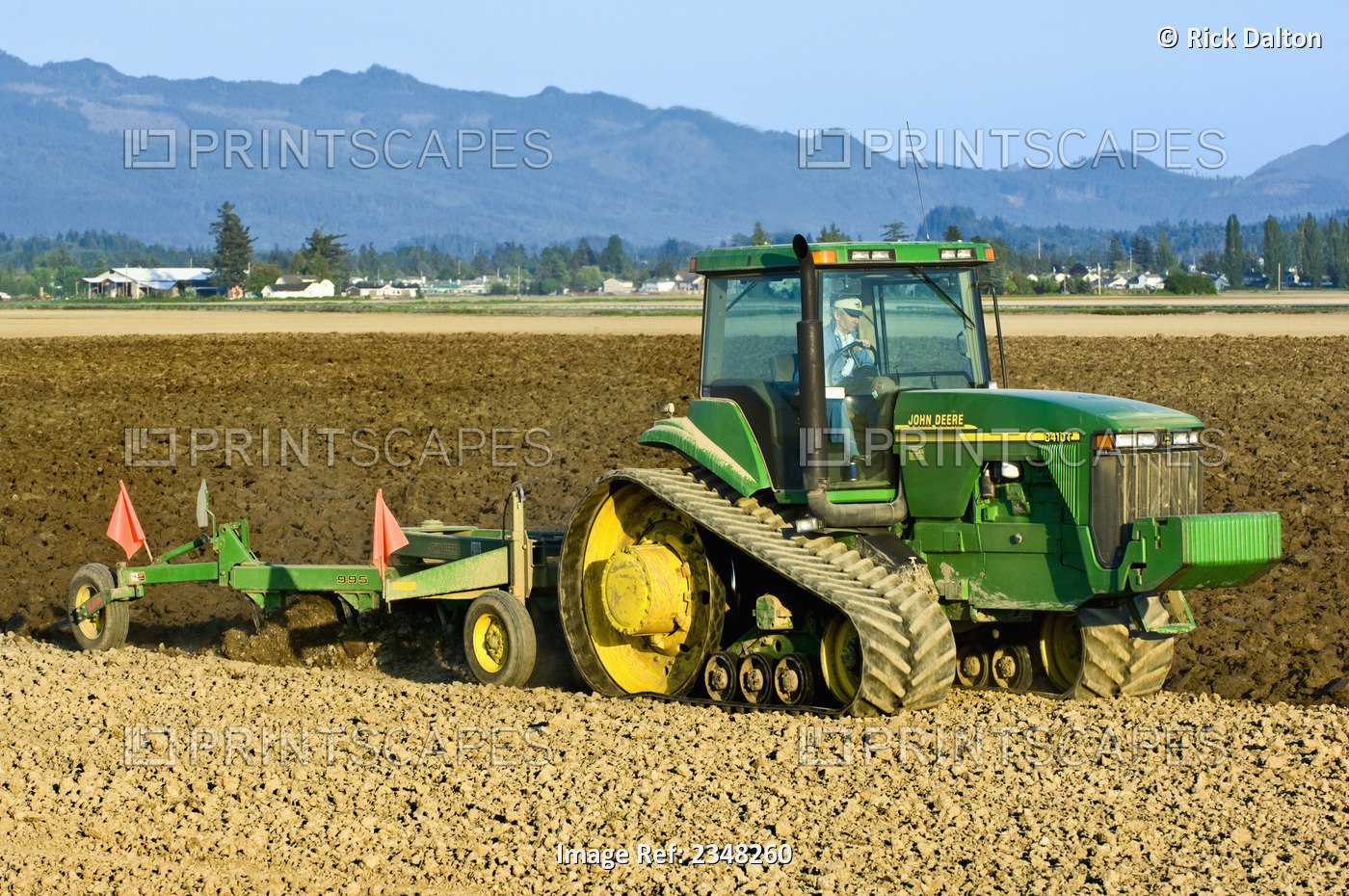 Agriculture - A John Deere tracked tractor pulling a reversible plow prepares a ...