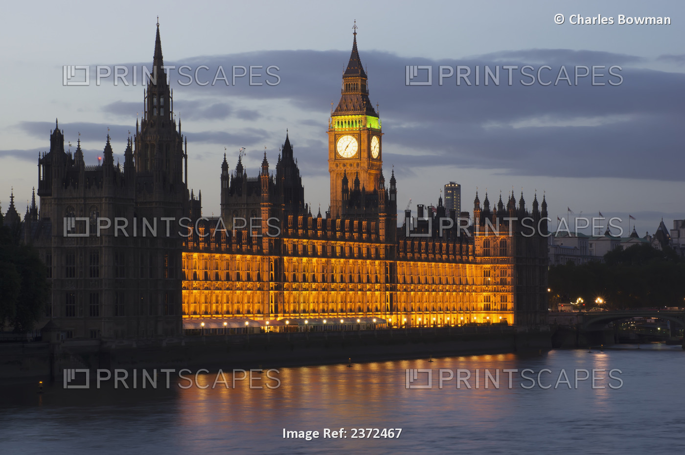 A Building And Clock Tower Along The Water's Edge Illuminated At Dusk; London, ...