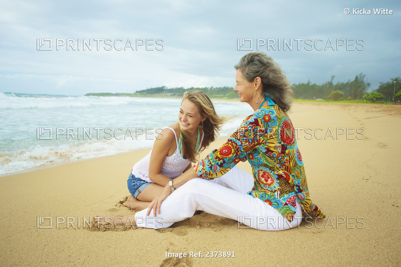 A Mother And Daughter Sitting Together On The Beach At The Water's Edge; Kauai, ...